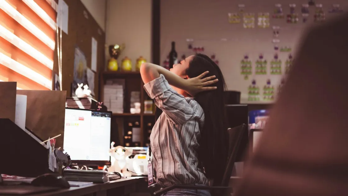 Office worker stretching at a desk, representing return to office pressure and hybrid missteps covered in this week’s remote work news about attendance-linked pay and metrics-driven RTO.