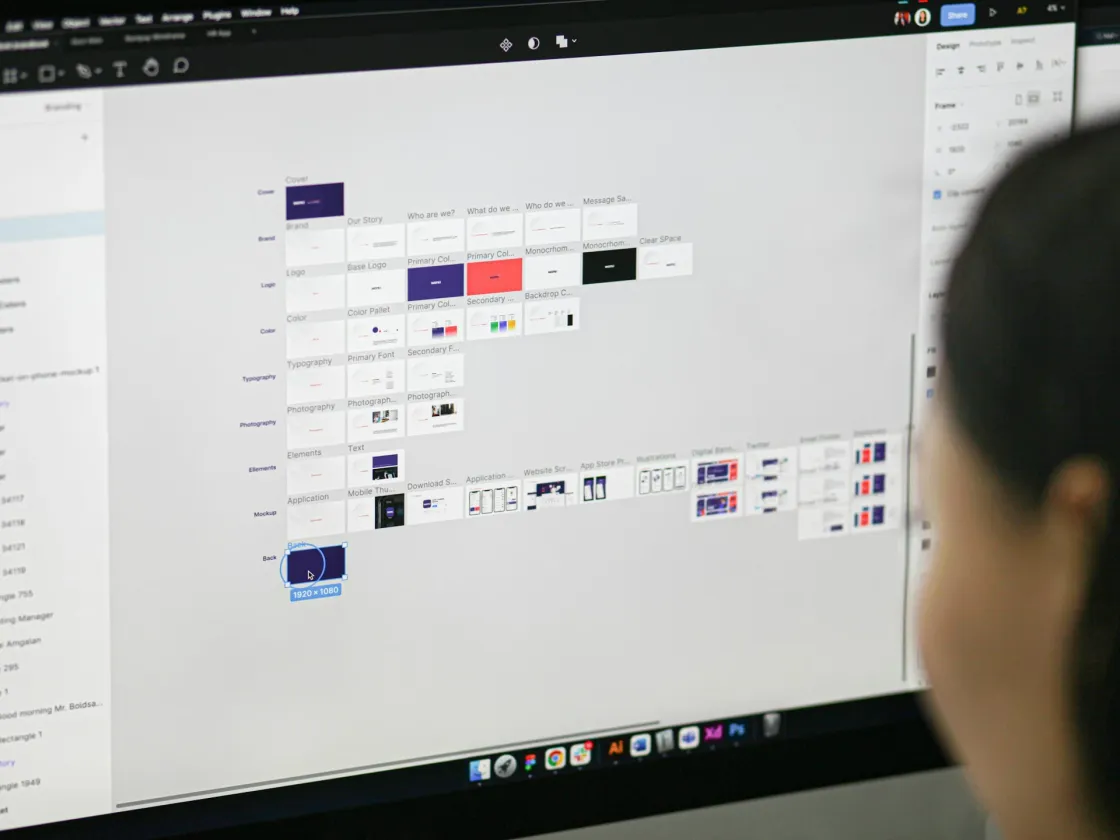 Close-up of a designer reviewing a Figma design system on a desktop monitor, with UI components and brand styles visible.