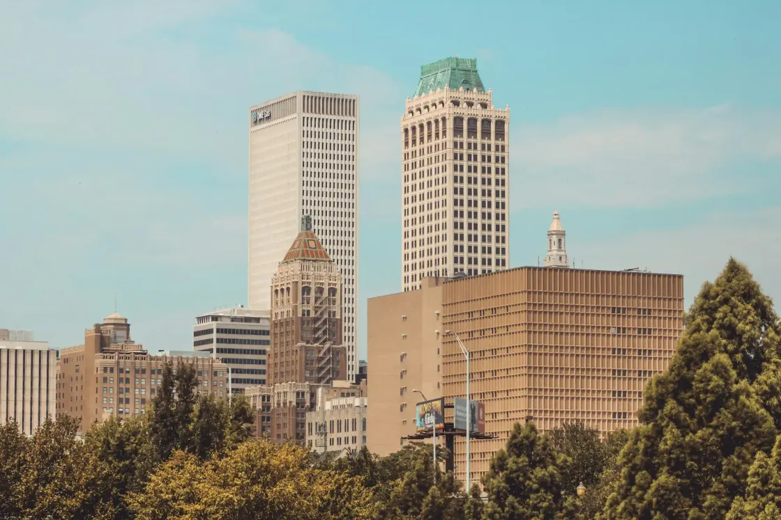 Downtown Tulsa, Oklahoma skyline with office towers rising above trees on a clear day.
