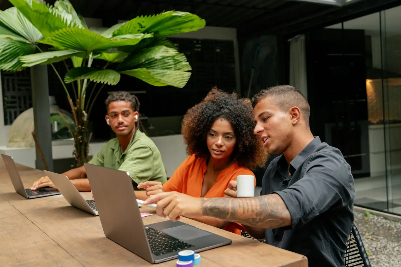 Small team collaborating on laptops in an open-air workspace, representing a hybrid work team planning cadence, core hours, and outcome-based metrics.